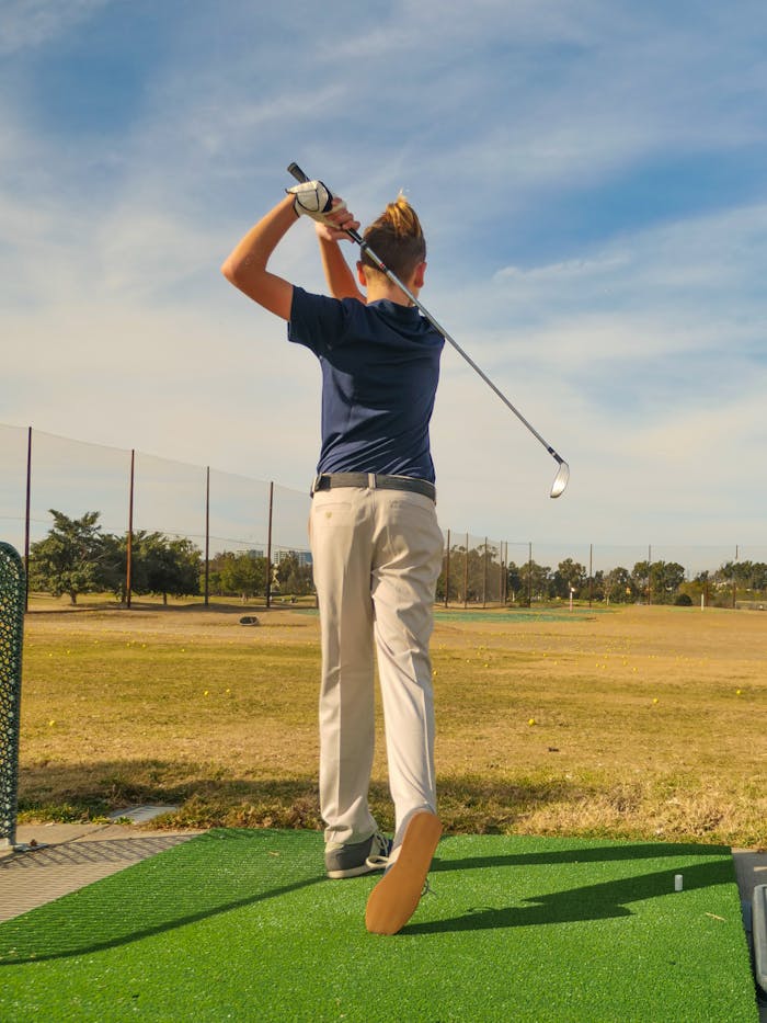 Rear view of a young golfer practicing swing at an outdoor driving range on a sunny day.
